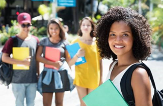 Young woman holding books with her fellow students standing behind her. 