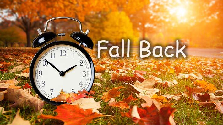 Fall leaves on the gross with an alarm clock and the words Fall Back.